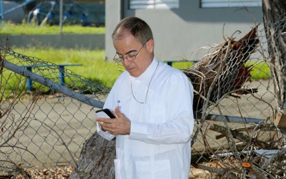 Archbishop Roberto González of San Juan, Puerto Rico, talks on his cellphone amid debris Oct. 25, more than one month after Hurricane Maria devastated the island. (CNS/Bob Roller)