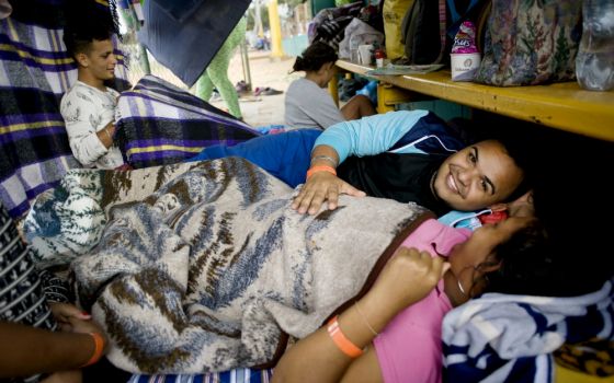 Tomas Torres puts his hand on the stomach of his pregnant wife, Elvia Perez de Torres, as they rest at a camp for migrants at a sports facility in Tijuana, Mexico. (CNS/David Maung)