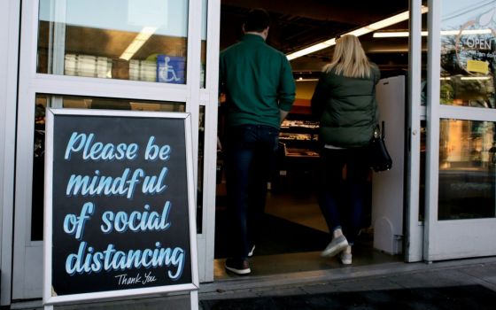 Shoppers enter a Seattle grocery store March 17 near a sign requesting social distancing, following reports of coronavirus cases in the area. (CNS/Reuters/David Ryder)