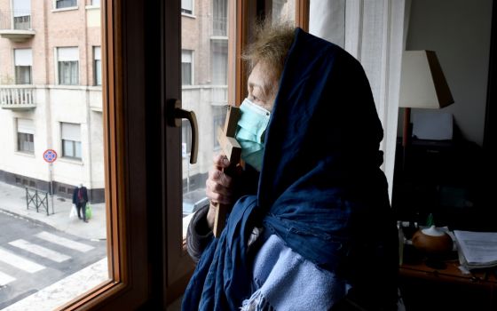 A woman wearing a protective face mask kisses a cross as she prays from the window of her home in Turin, Italy, March 25. (CNS/Reuters/Massimo Pinca)