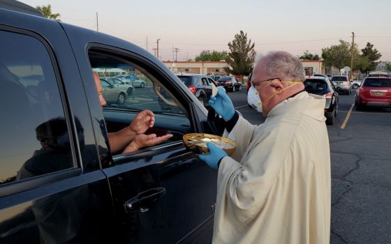 Bishop Peter Baldacchino wears a mask and gloves while giving Communion to a passenger of a vehicle during the Easter Vigil in the parking lot of the Cathedral of the Immaculate Heart of Mary in Las Cruces, New Mexico, April 11. (CNS)