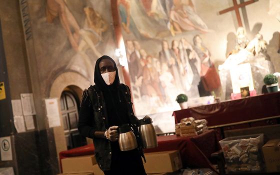 A volunteer carries coffee for people waiting for a free meal at the Church of Santa Anna in Barcelona, Spain, April 21, 2020, during the COVID-19 pandemic. (CNS/Reuters/Nacho Doce)