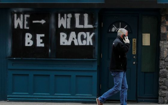 A man passes by a boarded-up restaurant in New York City April 29 with a sign suggesting it will reopen for business once it's safe in the coronavirus pandemic climate. (CNS/Reuters/Brendan McDermid)