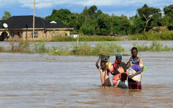 A boy and young man help a woman wade through floodwaters in Busia, Kenya, May 3, 2020. Some African Catholic advocates believe the church needs to do more to advance the ideas in Pope Francis' 2015 encyclical, "Laudato Si'." (CNS photo/Thomas Mukoya, Reu