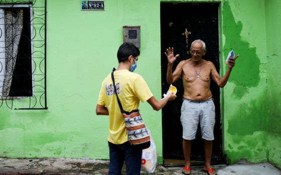 Seminarian Renan Alberto Lima de Oliveira, 21, assigned to Our Lady of Perpetual Help Catholic Church in Manaus, Brazil, delivers a protective mask to a resident in one of the city's slums May 21 to minimize the spread of COVID-19. (CNS/Reuters)