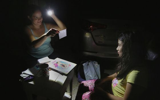 In this 2017 file photo, Margarita Rodriguez holds a flashlight as she quizzes her 11-year-old daughter Isel Martinez on homework outside their home in San Juan, Puerto Rico. (CNS/Bob Roller)