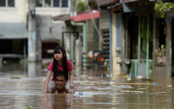 A man carries a child on his shoulders through a flooded street in Manila, Philippines, following Typhoon Vamco. (CNS/Reuters/Lisa Marie David)