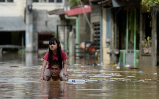 A man carries a child on his shoulders through a flooded street in Manila, Philippines, following Typhoon Vamco. (CNS/Reuters/Lisa Marie David)