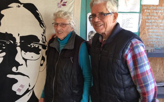 Mercy Sister Betty Campbell and Carmelite Fr. Peter Hinde pose next to an illustration of St. Oscar Romero in a 2019 photo in Ciudad Juarez, Mexico. Hinde died from complications due to COVID-19 Nov. 19, at the age of 97. (CNS/Julie Bourbon, courtesy of t