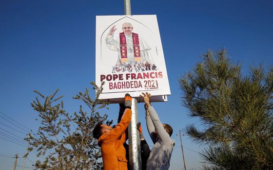 Volunteers secure a placard on a pole along a street in Qaraqosh, Iraq, Feb. 22. The placard shows the official logo, designed by Ragheed Nenwaya, for Pope Francis' planned March 7 visit to Qaraqosh, also known by its Aramaic name of Baghdeda.