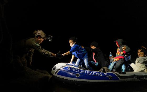 Migrants seeking asylum in the U.S. attempt to get off an inflatable raft with the help of a Texas Ranger officer April 5, 2021, in Roma, Texas, after they crossed the Rio Grande from Mexico. (CNS/Go Nakamura, Reuters)