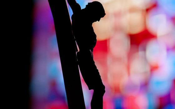 A crucifix is silhouetted against a stained-glass window in this illustration photo. (CNS/Mike Crupi, Catholic Courier)