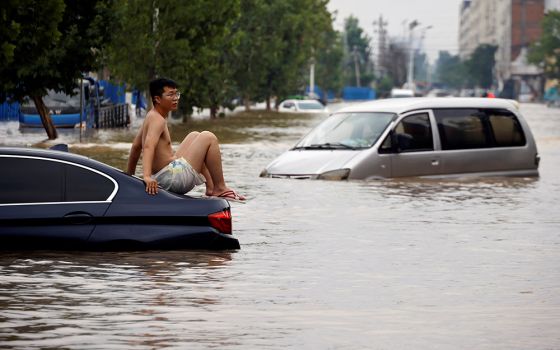 A man sits on a stranded vehicle on a flooded road following heavy rainfall in Zhengzhou, China, July 22. (CNS/Reuters/Aly Song)