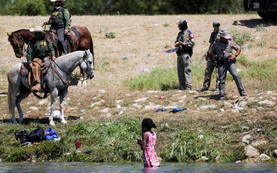 U.S. law enforcement officers in Del Rio, Texas, stand near a young migrant woman bathing in the Rio Grande Sept. 19. (CNS/Reuters/Daniel Becerril)