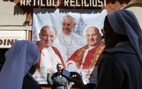 Nuns from Brazil take photos in front of a large banner of Pope Francis, then-Blesseds John XXIII and John Paul II in Rome in this April 25, 2014, file photo. With the news that Pope John Paul I will be beatified, some have begun to wonder if being pope i