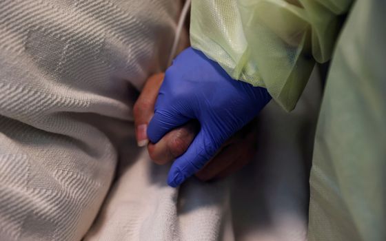 A woman at Madison Memorial Hospital in Rexburg, Idaho, holds the hand of a COVID-19 patient in her isolation room Oct. 28, 2021. (CNS/Reuters/Shannon Stapleton)