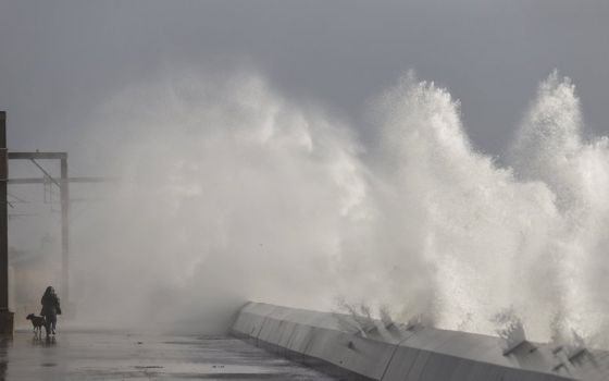 A man walks his dog in February 2020 as waves crash against a seawall in Saltcoats, in Scotland, the country where the U.N. climate conference is scheduled to end Nov. 12. (CNS photo/Eddie Keogh, Reuters)