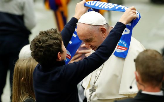 A boy gives Pope Francis a scarf of the Pavia soccer club during the weekly general audience in the Paul VI hall at the Vatican Nov. 17, 2021. (CNS photo/Remo Casilli, Reuters)