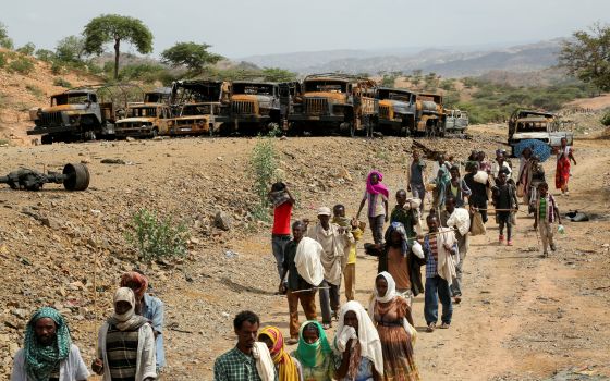 Villagers returning from a market in the town of Yechila walk past scores of burned vehicles in Ethiopia's Tigray region July 10, 2021. (CNS photo/Giulia Paravicini, Reuters)
