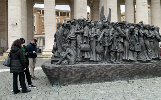 Visitors to St. Peter's Square use their smartphones to read about the sculpture "Angels Unawares" by Canadian sculptor Timothy Schmalz Dec. 28, 2021. (CNS photo/Cindy Wooden)