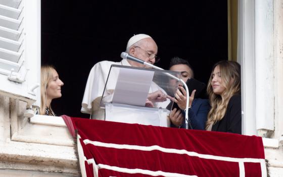 Young people from Portugal join Pope Francis in the window of his studio overlooking St. Peter's Square Oct. 23, 2022, as they help him use a tablet to be the first to register to attend World Youth Day 2023 in Lisbon.