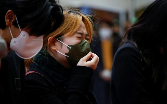 A South Korean woman wearing a mask cries beside another person wearing a mask