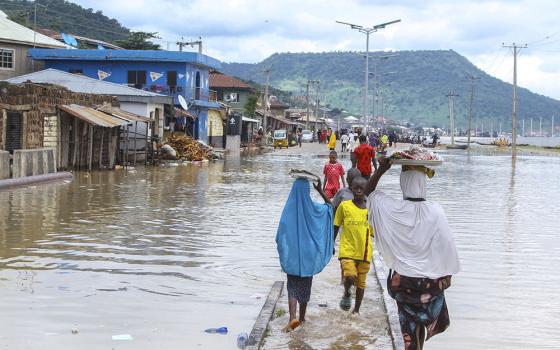 People walk through floodwaters following several days of downpours in Kogi, Nigeria, Oct. 6. Officials in Nigeria have called the floods the country's worst in more than a decade, blaming the disaster on heavy rainfall and the release of excess water from the Lagdo Dam in neighboring Cameroon. (AP/Fatai Campbell)