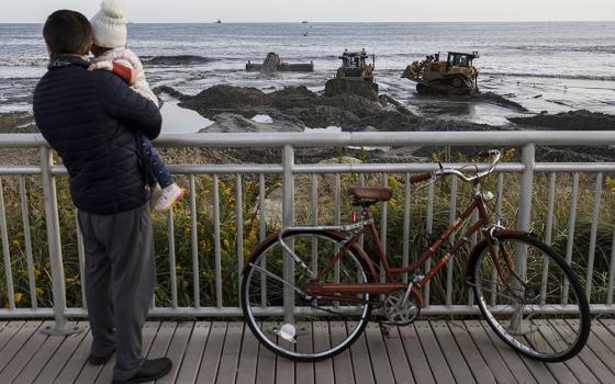 People watch sand dredging work Oct. 22 in the Far Rockaway neighborhood of the Queens borough of New York. The U.S. Army Corps of Engineers' Atlantic Shorefront Resiliency Project aims to construct a reinforced dune system designed to block storm surge. (AP/Julia Nikhinson)