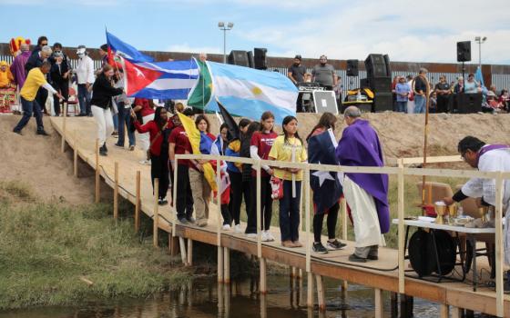 Migrants with flags line up on a bridge across the Rio Grande to receive communion from Bishop Mark Seitz 