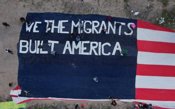 A banner of a US flag that says "We the migrants built America" stands in a parking lot