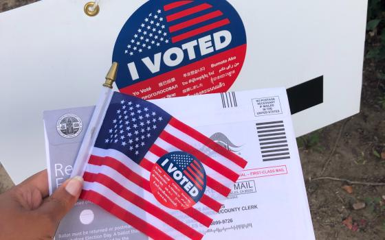 A sign, postcard and American flag with "I voted" stickers on them. (Unsplash/Janine Robinson)