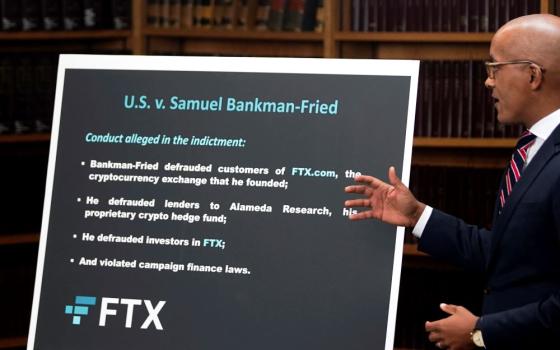 Man points to sign with list of charges against CEO of FTX.