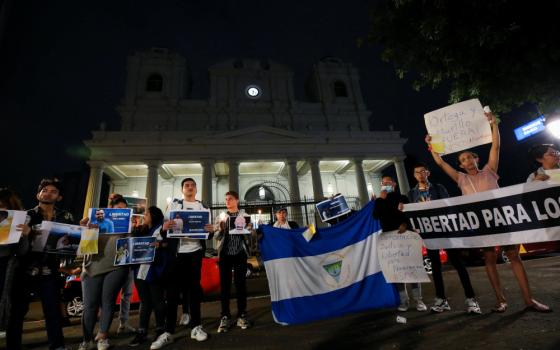 People carry the Nicaraguan flag and protest signs outside an embassy in the dark