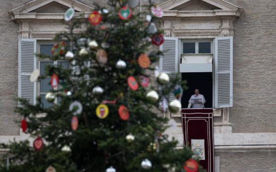 A Christmas tree stands in the foreground as Pope Francis appears in a Vatican window