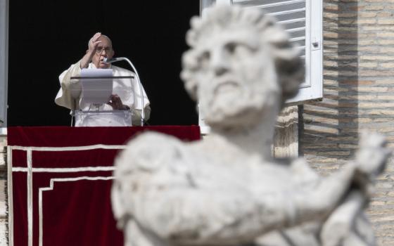 Pope Francis raises one hand over a podium with a piece of paper in the window of his apartment