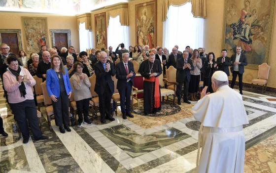Pope Francis stands in front of a large group of people in the Vatican