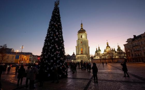 A tall Christmas tree stands in a plaza in front of a church at twilight