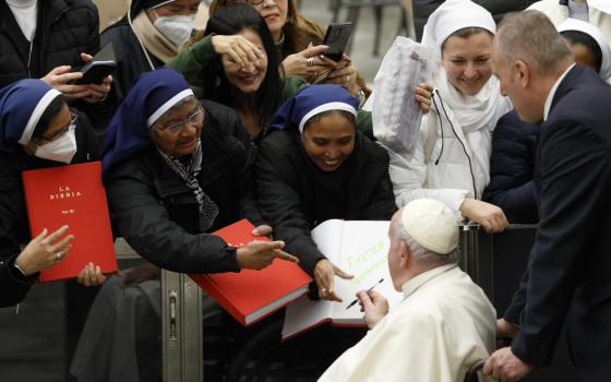 The pope signs a sister's red Bible as she stands among other sisters