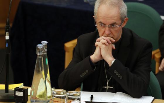 Justin Welby sits in a chair at a table with his hands folded in front of his face