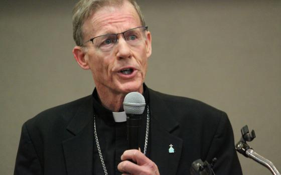 A white middle-aged bishop with glasses holds a microphone
