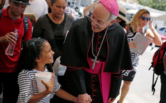 Bishop Mark J. Seitz of El Paso, Texas, shares a smile with a Honduran girl named Cesia as he walks and prays with a group of migrants at the Lerdo International Bridge in El Paso June 27, 2019. (CNS photo/Jose Luis Gonzalez, Reuters)
