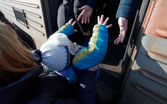 A child is assisted as evacuees board a train before leaving the separatist-controlled city town of Makiivka outside Donetsk, Ukraine, Feb. 22, 2022. (CNS photo/Alexander Ermochenko, Reuters)