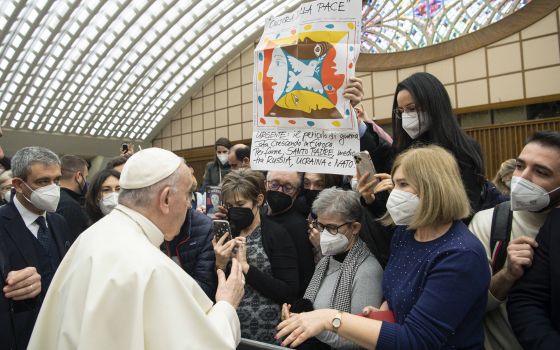 Pope Francis greets people near a banner in Italian calling for the pope's intervention with Russia, Ukraine and NATO, during his general audience in the Paul VI hall at the Vatican Jan. 19, 2022. (CNS photo/Vatican Media)