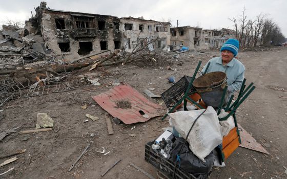 A woman pushes a cart with her belongings past buildings damaged during the Russian war in the separatist-controlled town of Volnovakha, Ukraine, March 15, 2022. (CNS photo/Alexander Ermochenko, Reuters)
