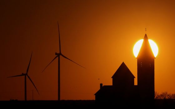 Power-generating windmill turbines and a church are pictured during sunset at a wind park near Cambrai, France, March 18, 2022. (CNS/Reuters/Pascal Rossignol)