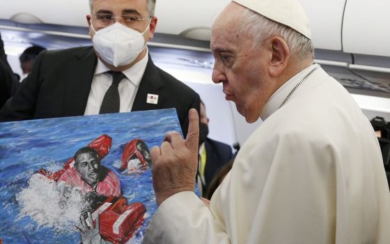 Pope Francis gestures as he looks at artwork presented by a journalist on his flight from Rome to Malta April 2, 2022. 