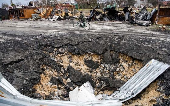A local resident rides a bicycle past a bomb crater as Russia's attack on Ukraine continues in the village of Demydiv, outside Kyiv, Ukraine, April 6. (CNS/Reuters/Vladyslav Musiienko)