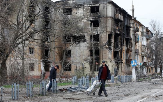 People walk past destroyed apartments in the southern port city of Mariupol, Ukraine, April 18, 2022, during the Russian war. (CNS photo/Alexander Ermochenko, Reuters)