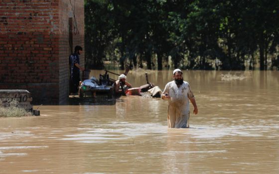 A man wades through floodwaters trying to salvage his belongings following heavy rains during the monsoon season in Charsadda, Pakistan, Aug. 28, 2022. (CNS photo/Fayaz Aziz, Reuters)