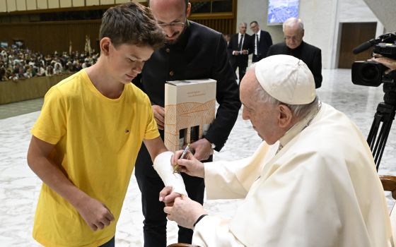 Pope Francis autographs the cast of a boy during his general audience in the Paul VI hall at the Vatican Aug. 31, 2022. 